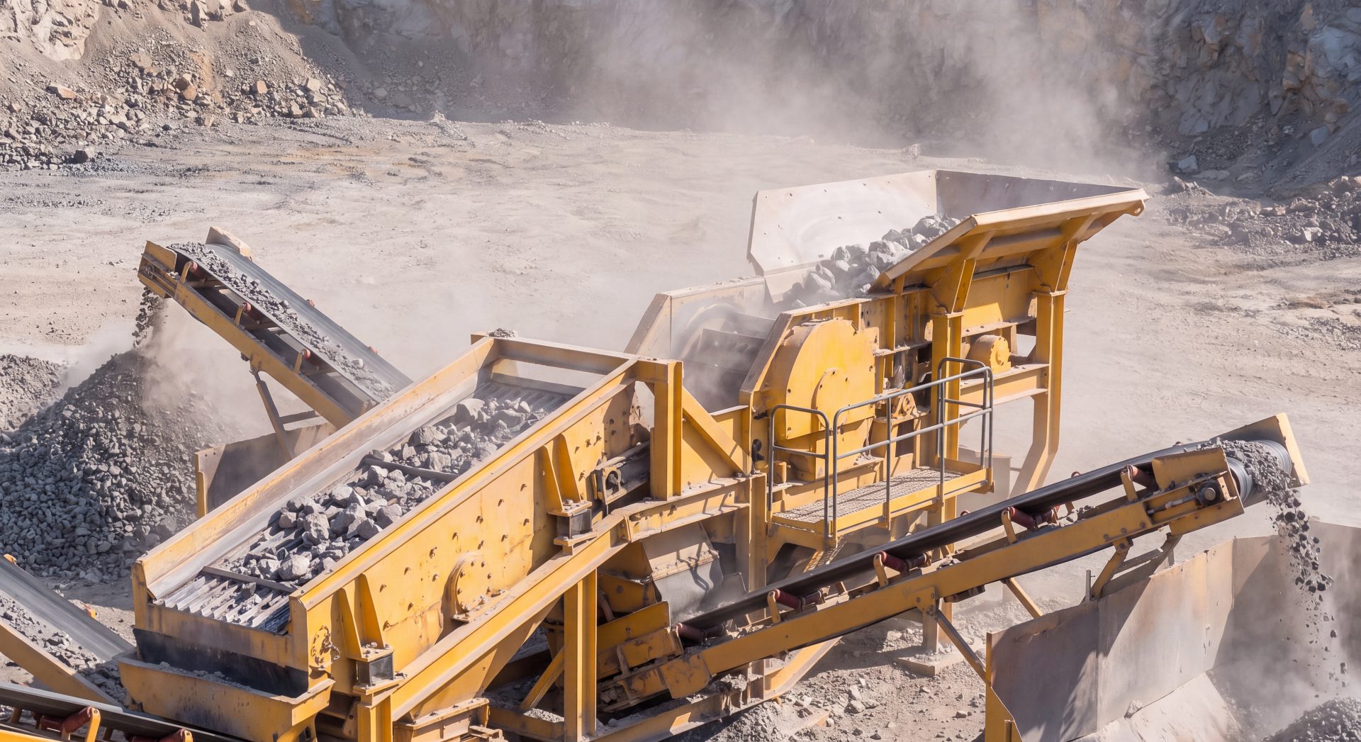 Mobile rock crusher and vibrating screen machine processing raw stones and gravel in an open cast mining quarry environment.