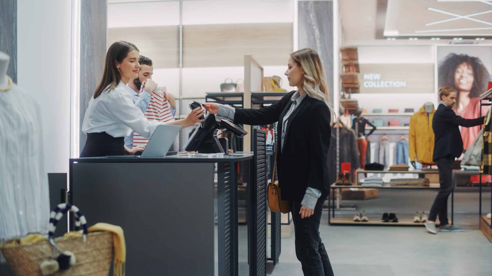 Clothing Store Checkout Cashier Counter: Beautiful Young Woman Buys Blouse from Friendly Retail Sales assistant, Paying with Contactless Credit Card. Fashion Shop with of Designer Brands.