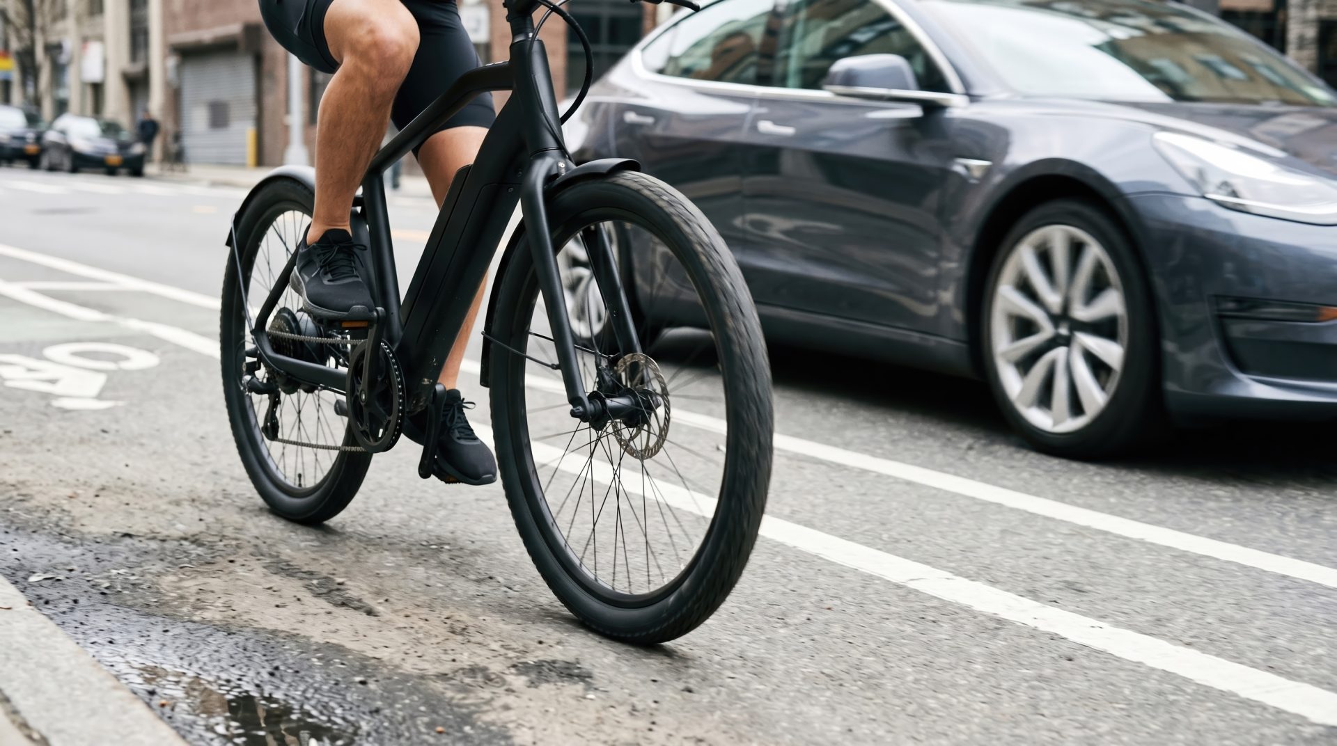 A young male adult riding a modern black electric bicycle in a city bike lane beside a car